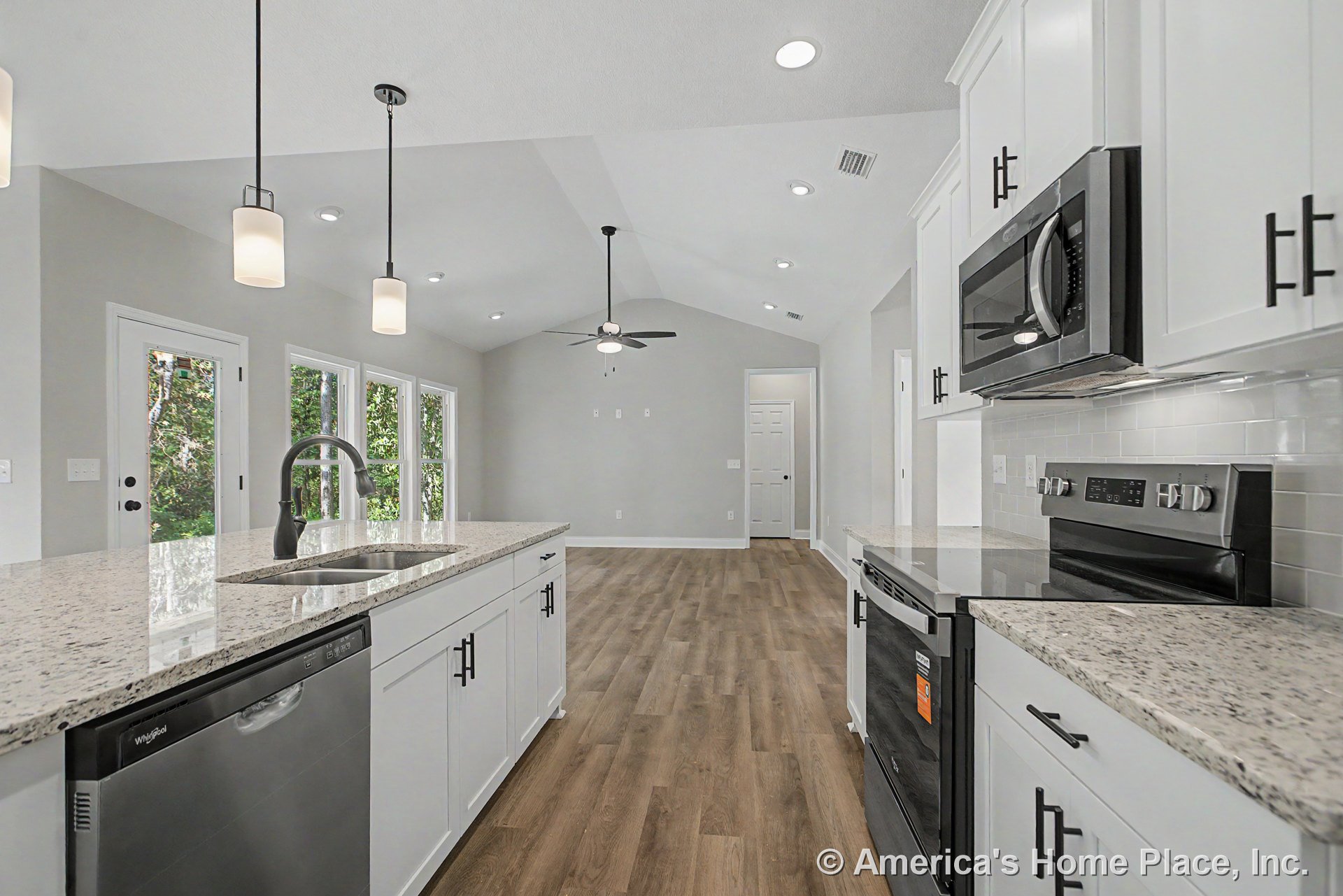 White shaker kitchen cabinets and granite island with stainless steel appliances, pendant and recessed lighting, wood-look flooring, vaulted ceiling with ceiling fan, large