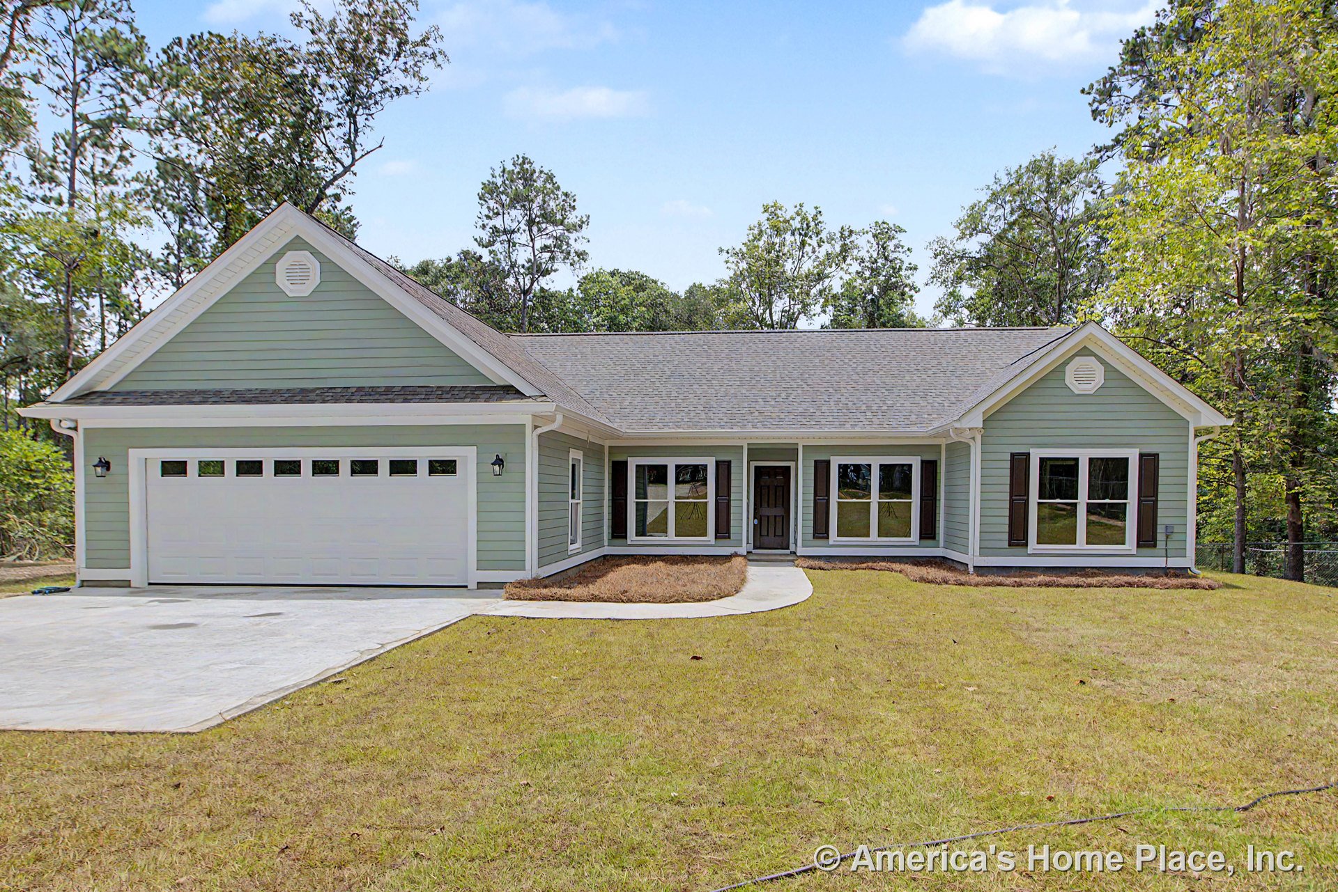 Light green horizontal siding with white trim and gutters, covered front porch, attached two-car garage with white door, multiple large windows with shutters, dark roof shingles