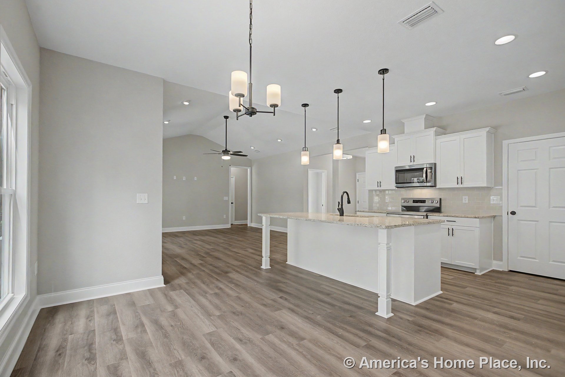 Open kitchen with white shaker cabinets, granite island countertop, pendant and recessed lighting, wood-look flooring, stainless steel appliances, and large windows.