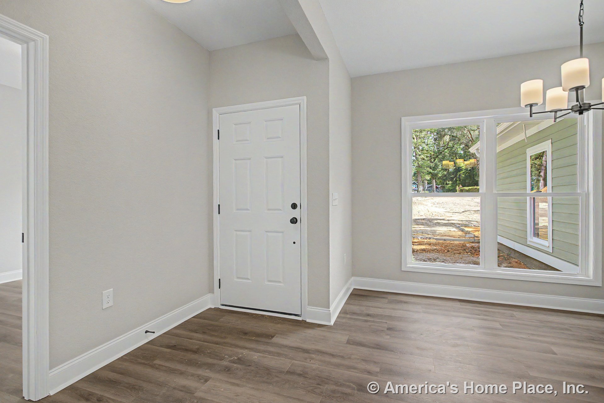 White paneled front door and large picture window in foyer with wood-look flooring, neutral wall paint, white baseboard trim, and modern chandelier lighting.