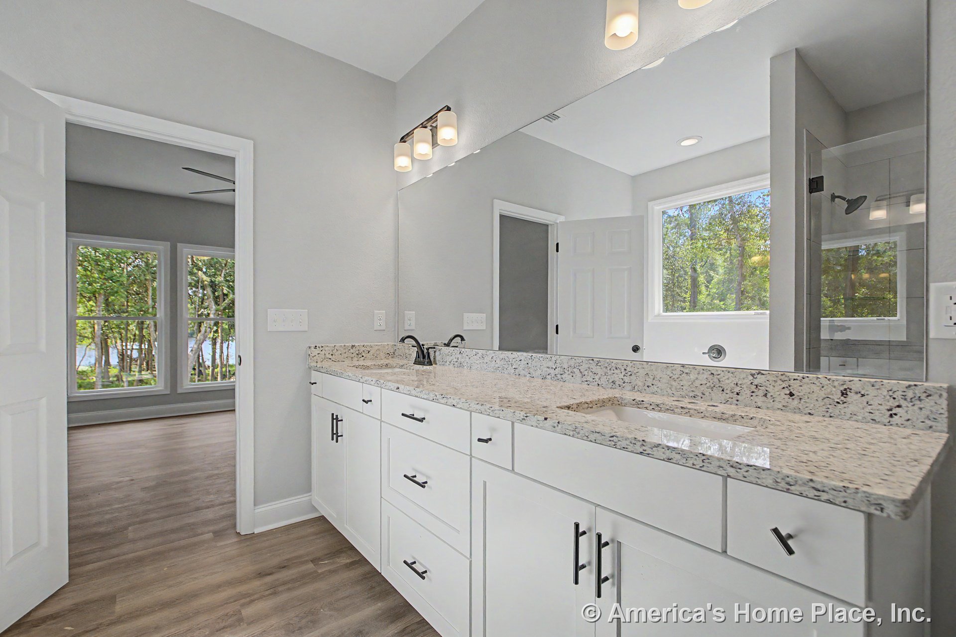 Double vanity with granite countertops and white shaker cabinets, large wall mirror with built-in vanity lighting, walk-in shower with glass door, wood-look flooring, modern