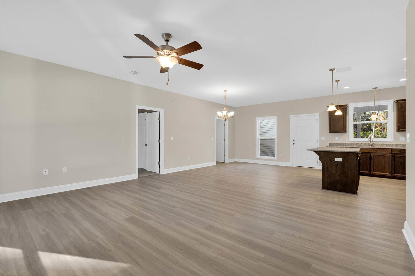 Spacious living room featuring hardwood floors, ceiling fan with light fixture, white walls with slatted accents, white door with black knobs, and marble countertop cabinetry