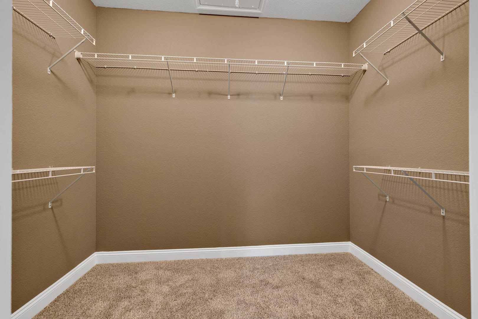 Walk-in closet with white wire shelving, metal hanging rod, and beige carpet flooring