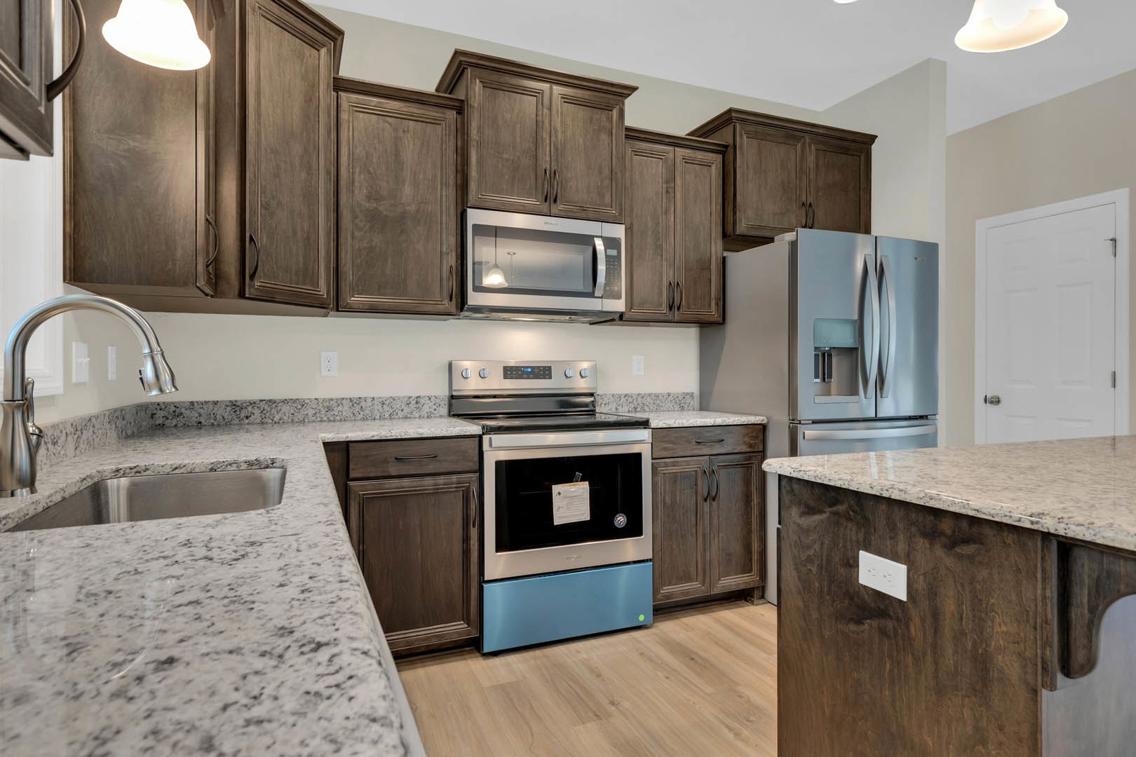 Granite countertops, stainless steel appliances, white cabinetry, built-in microwave, and modern stove in a custom kitchen