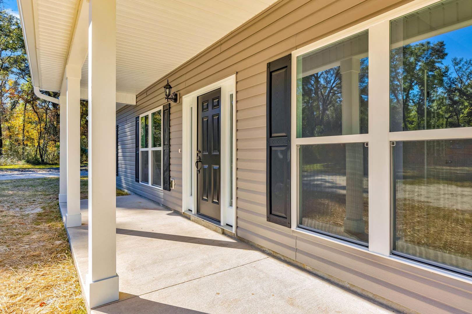 Wide front porch with white columns, black door, large windows, and shaded entry surrounded by mature trees