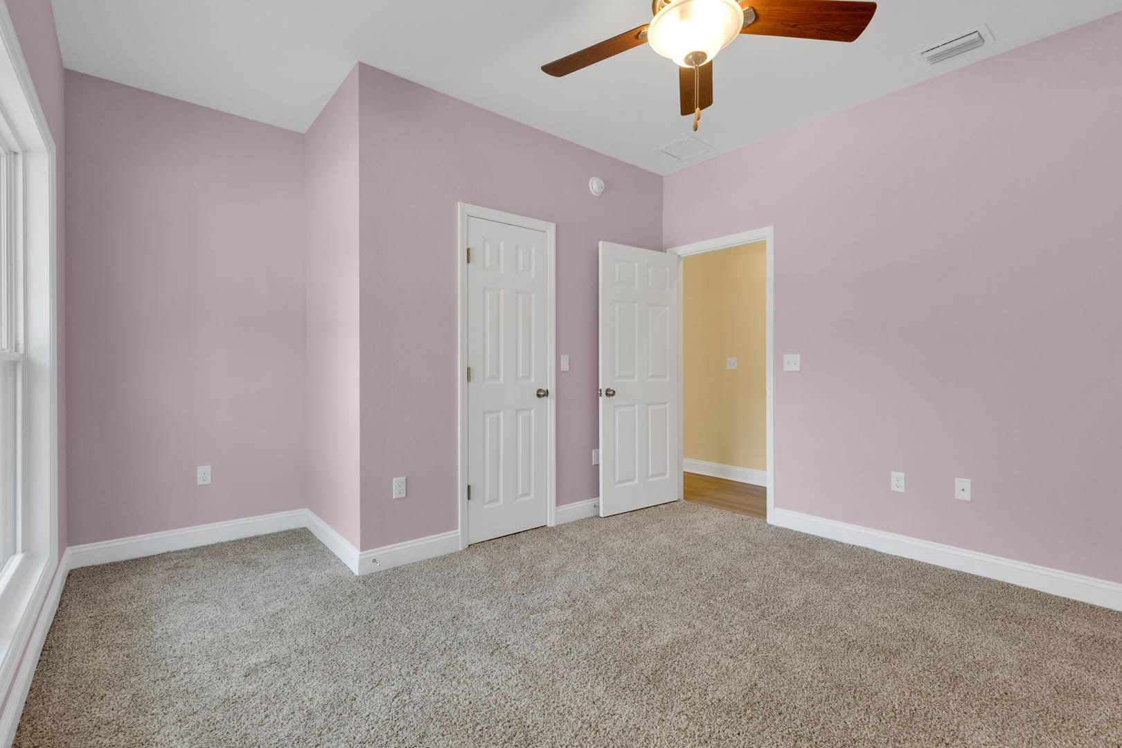Pink-walled room with white doors, silver door knob, carpeted floor, ceiling fan, light fixture, and light switch on wall