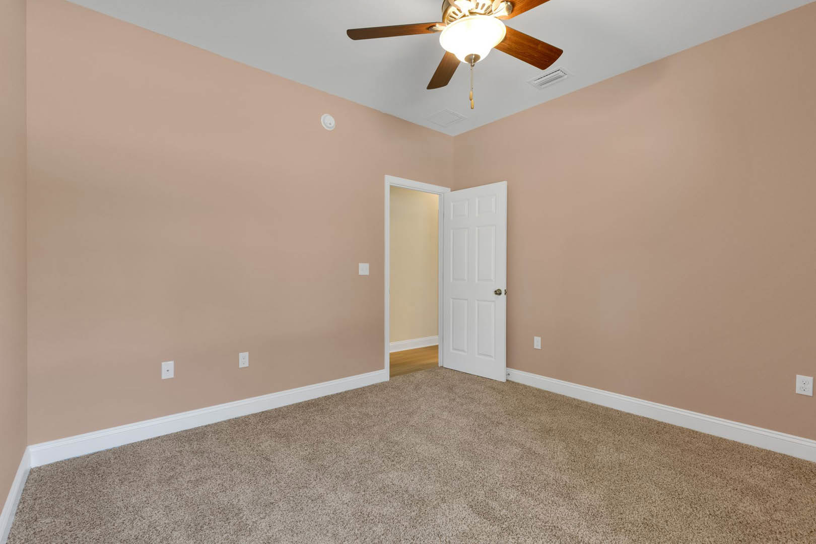 Carpeted room with white walls and trim, ceiling fan with light fixture, white door featuring gold knob, partial view of wood flooring