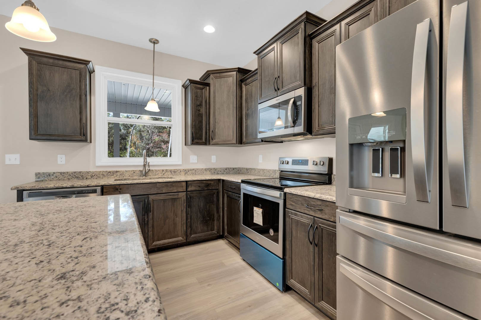 Granite countertops with black speckled surface, stainless steel refrigerator with two phones on top, microwave oven emitting light, wooden cabinetry, sink, and close-up of wooden