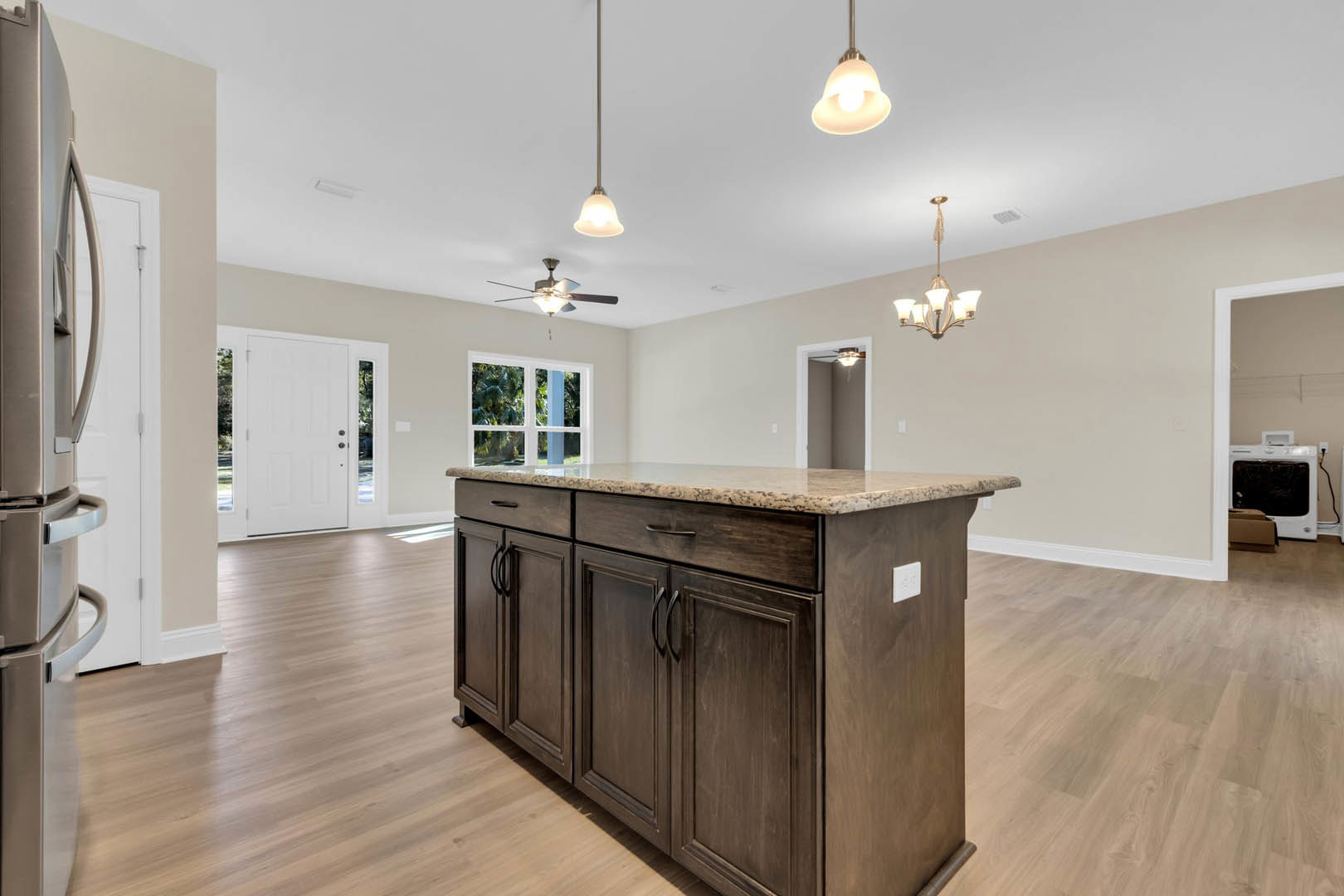 Granite kitchen island with brown cabinetry, white electrical outlet, stainless steel refrigerator, glass-paneled white door, and white television in adjacent room.