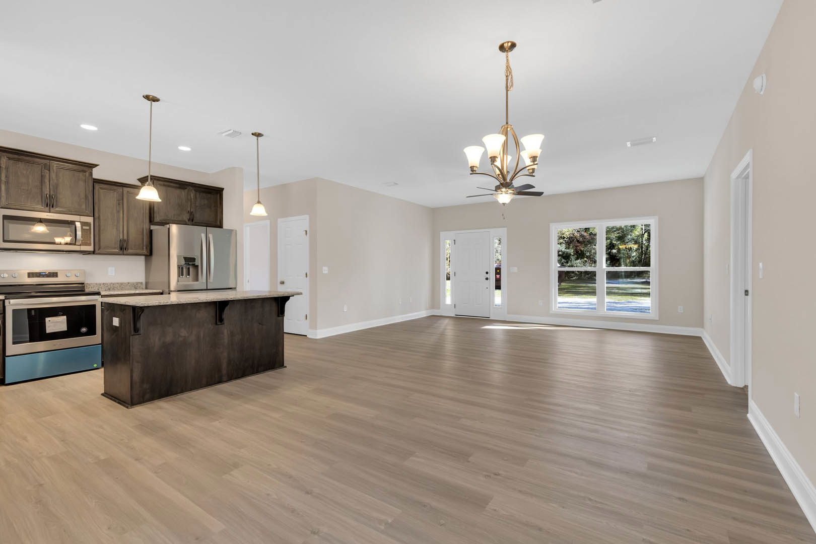 Spacious open-concept kitchen featuring a central island, wood flooring, white cabinetry, stainless steel appliances, and large windows overlooking a green lawn