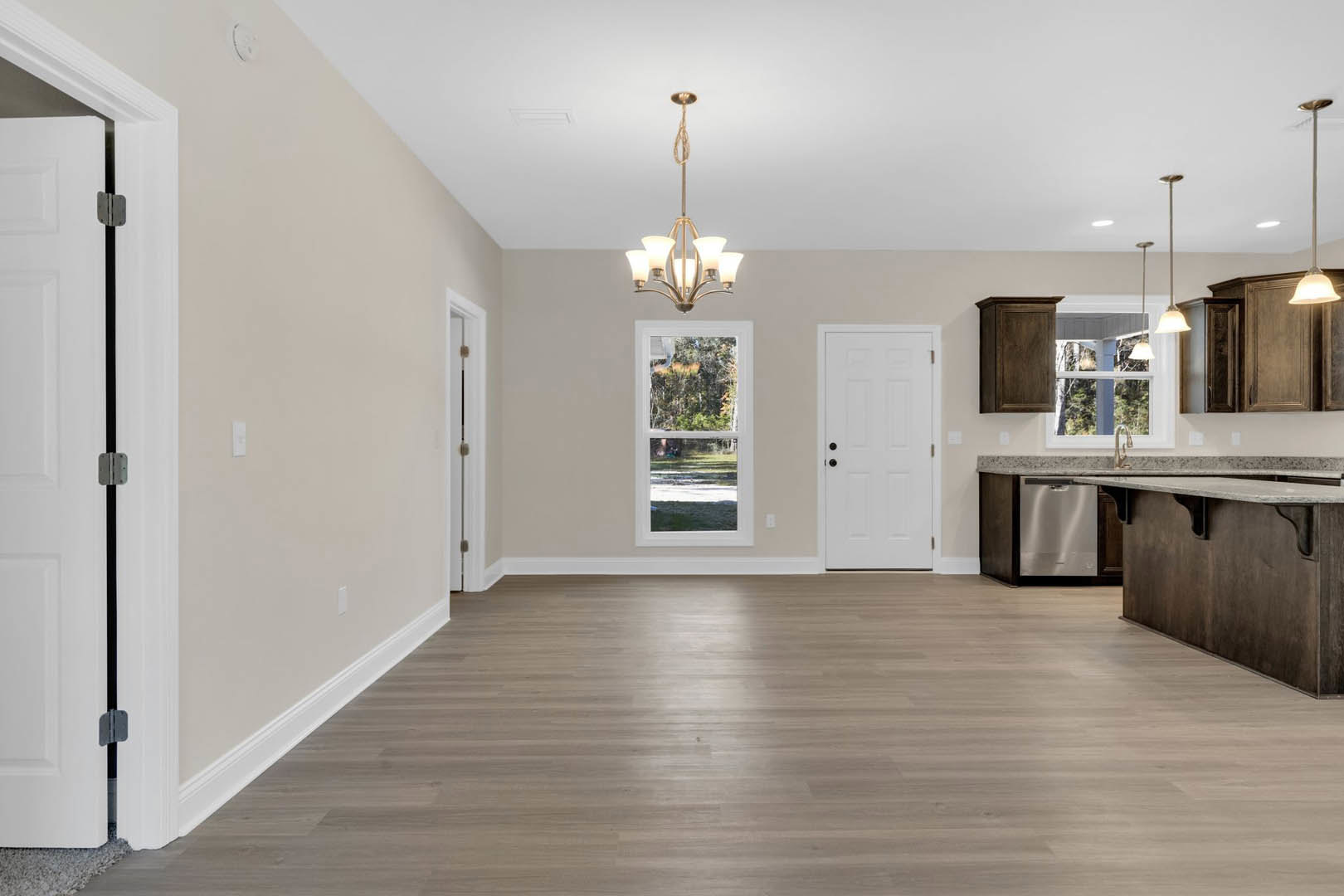 Hardwood floor room with white door featuring black knobs and hinge, large window showing trees outside, ornate chandelier hanging from ceiling, neutral walls, partial view of