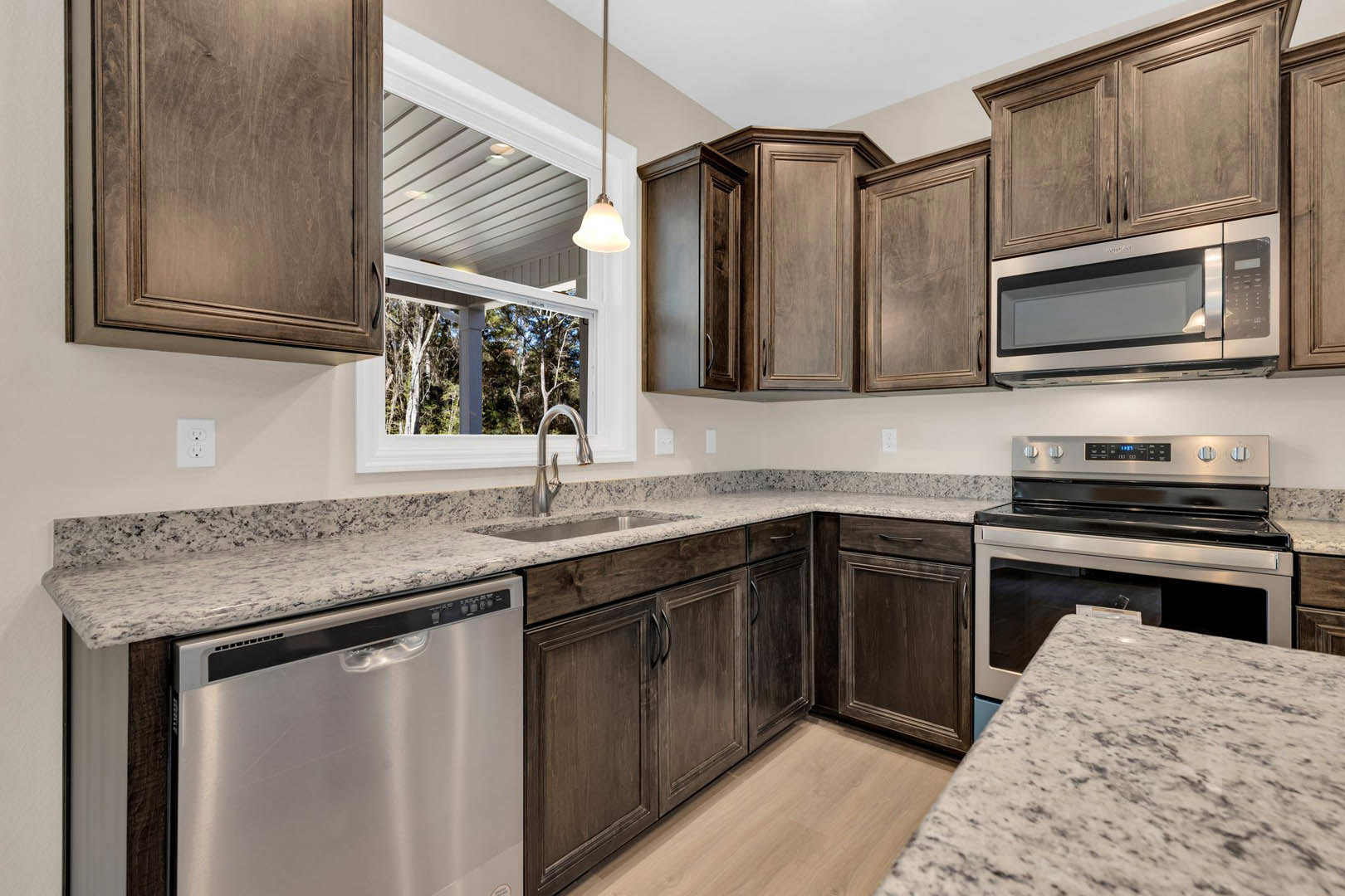 Granite countertops, stainless steel appliances including microwave, dishwasher, and glass-door stove, white electrical outlet, close-up of wooden cabinetry in a modern kitchen