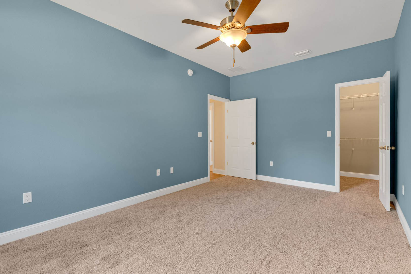 Blue-painted walls, white ceiling with a ceiling fan and light fixture, white closet and entry doors, beige carpeted floor