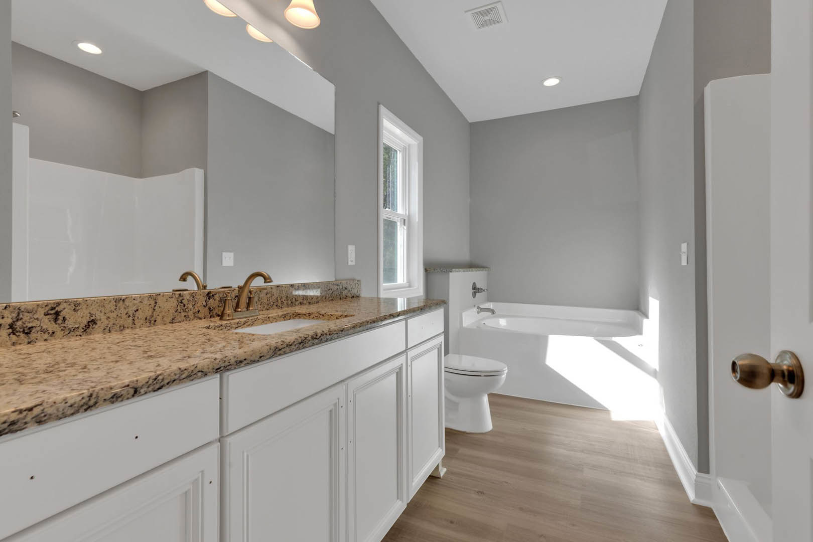 Bathroom featuring marble countertops, freestanding tub, white toilet, wooden flooring, tile walls, and modern sink with chrome tap