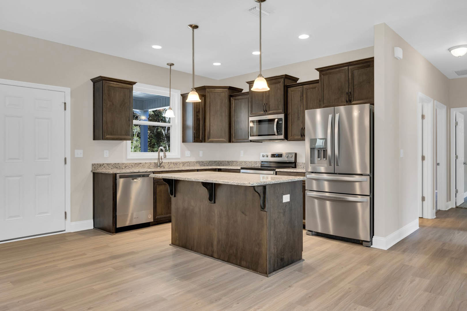 Spacious kitchen featuring a marble-topped island, stainless steel refrigerator and microwave, white cabinetry, metal hardware, and a window overlooking trees