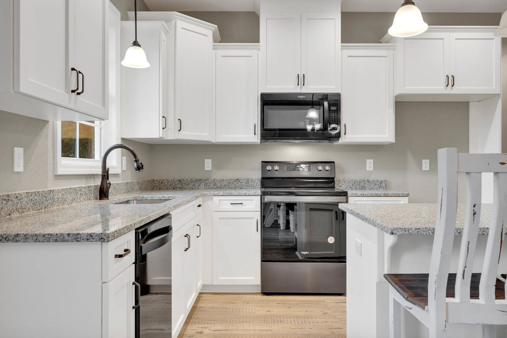 White kitchen cabinets with granite countertops, stainless steel sink, black microwave, wood flooring, and modern lighting fixtures
