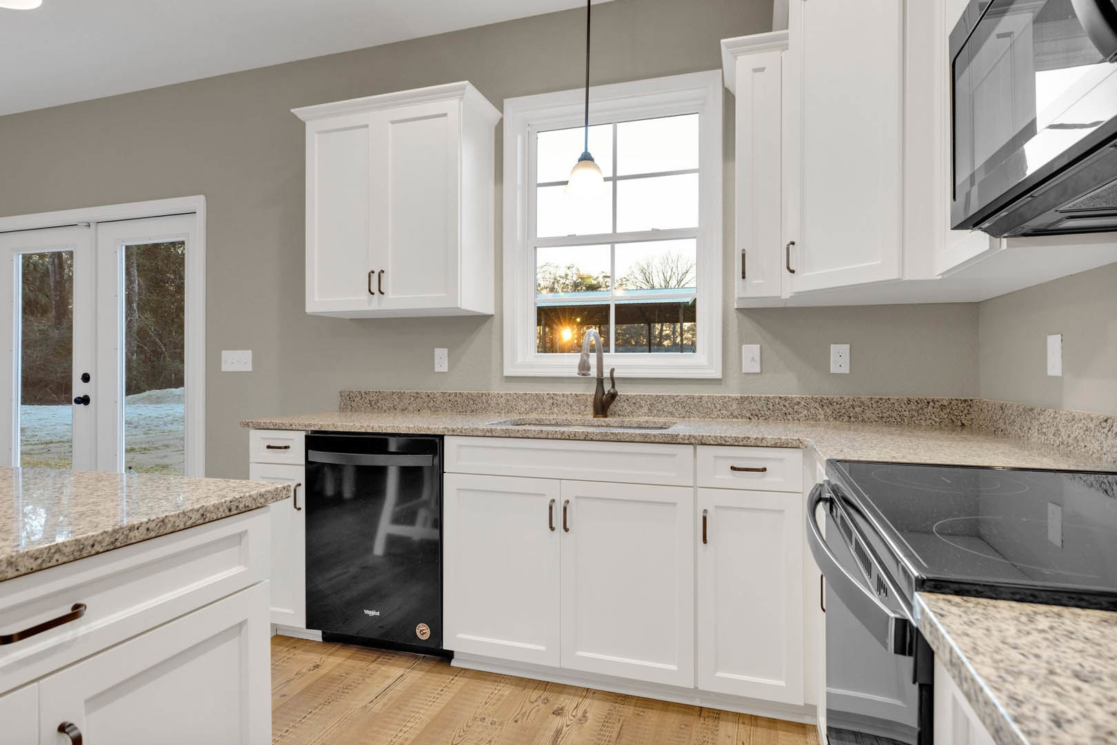 White kitchen cabinets with brushed metal handles, granite countertops, stainless steel microwave, double glass doors, and overhead ceiling light.