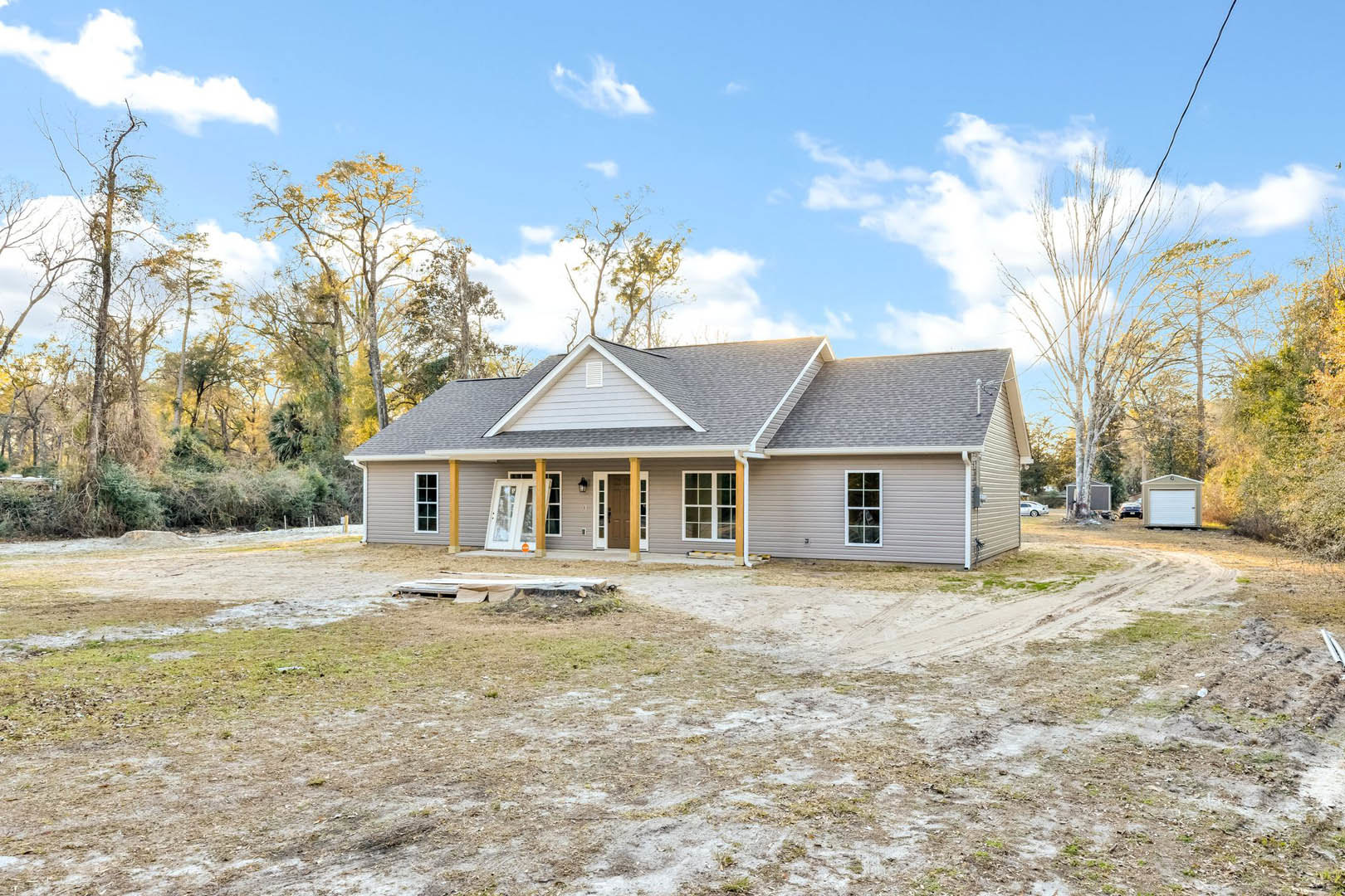 Partially built house with white framed windows, glass paneled door, covered porch, surrounded by dirt field under cloudy sky