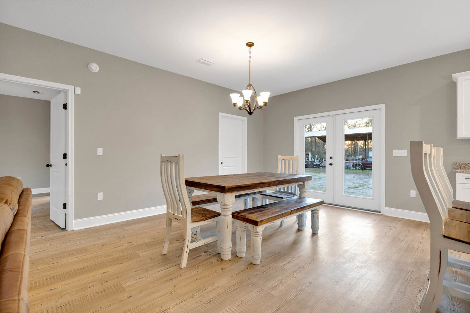 Wood dining table with upholstered chairs on hardwood flooring, glass-paneled double doors, white accent chair, modern chandelier, neutral walls