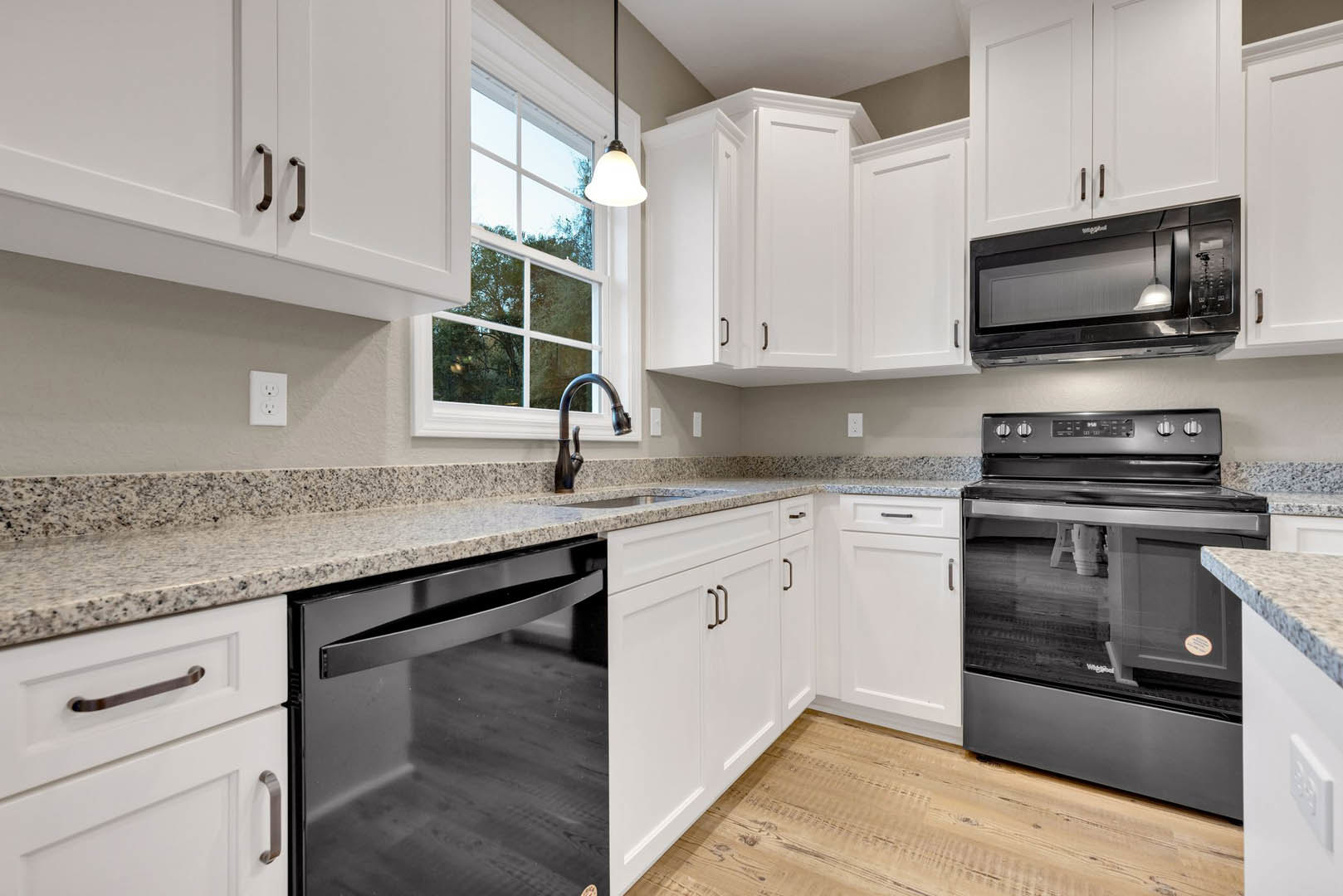 White kitchen with shaker cabinets, black appliances including stove, microwave, and dishwasher, marble countertop, stainless sink, modern light fixture, and white electrical