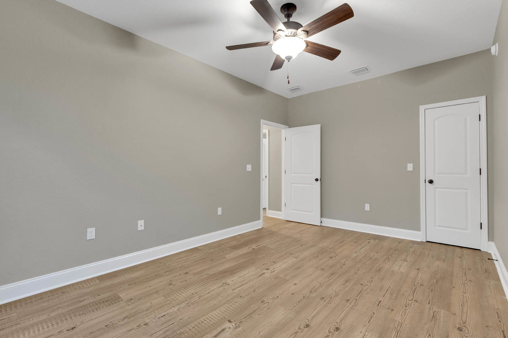 Ceiling fan with light fixture, wood laminate flooring, white walls with white trim, white door featuring black handle