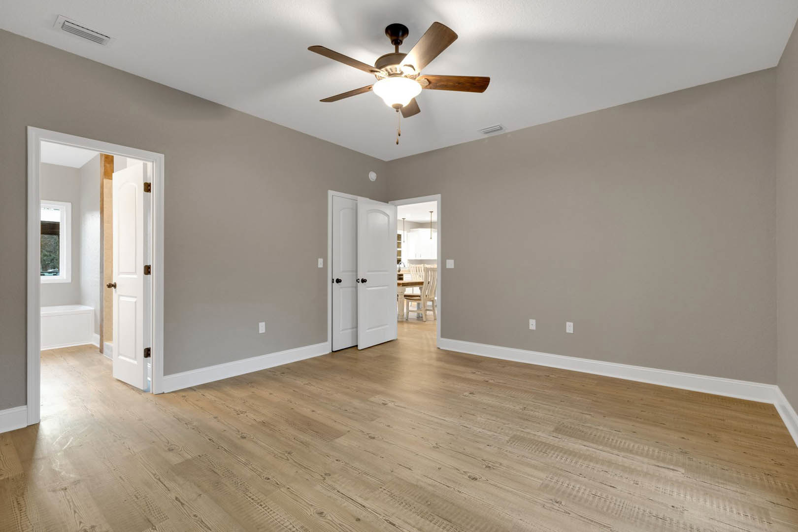 Ceiling fan with integrated light fixture, wood flooring, white paneled door with black hardware, smooth plaster walls and ceiling
