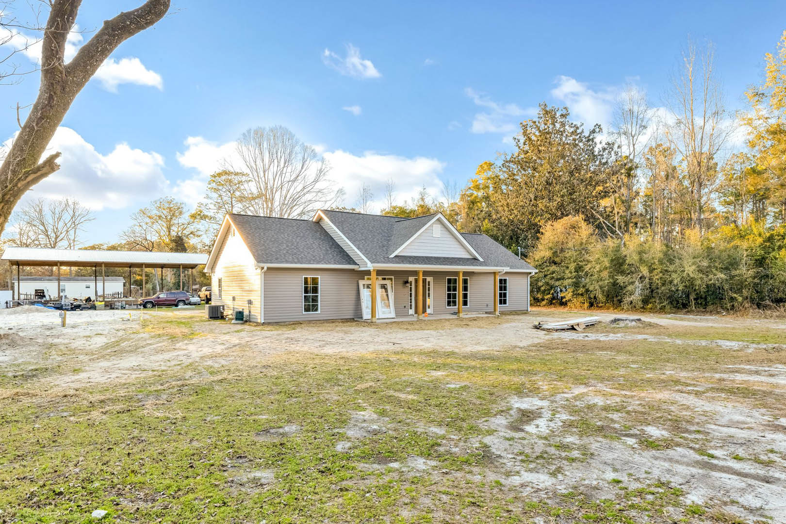 White farmhouse with open front door, surrounded by lush grass lawn, mature trees, and blue sky with scattered clouds; yellow pole near entrance.