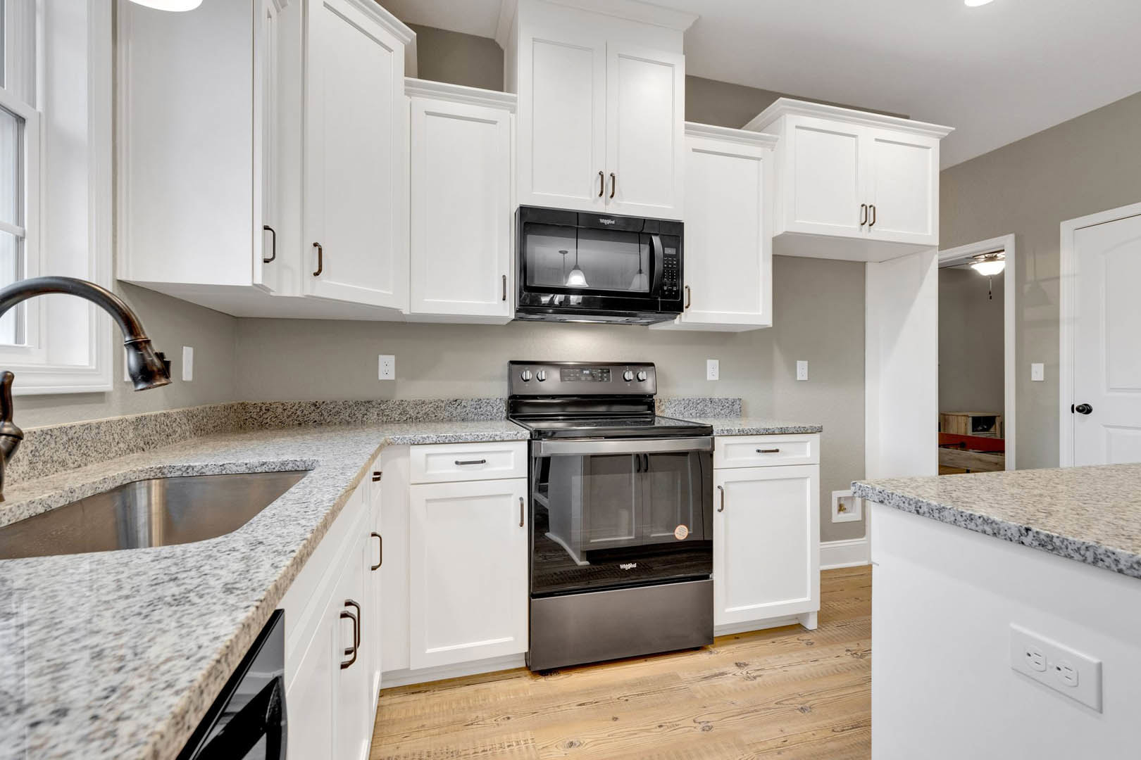 White kitchen cabinets, black appliances including microwave and stove, glass-front cabinet with sticker, white door with black handle, stainless steel sink, light countertops.