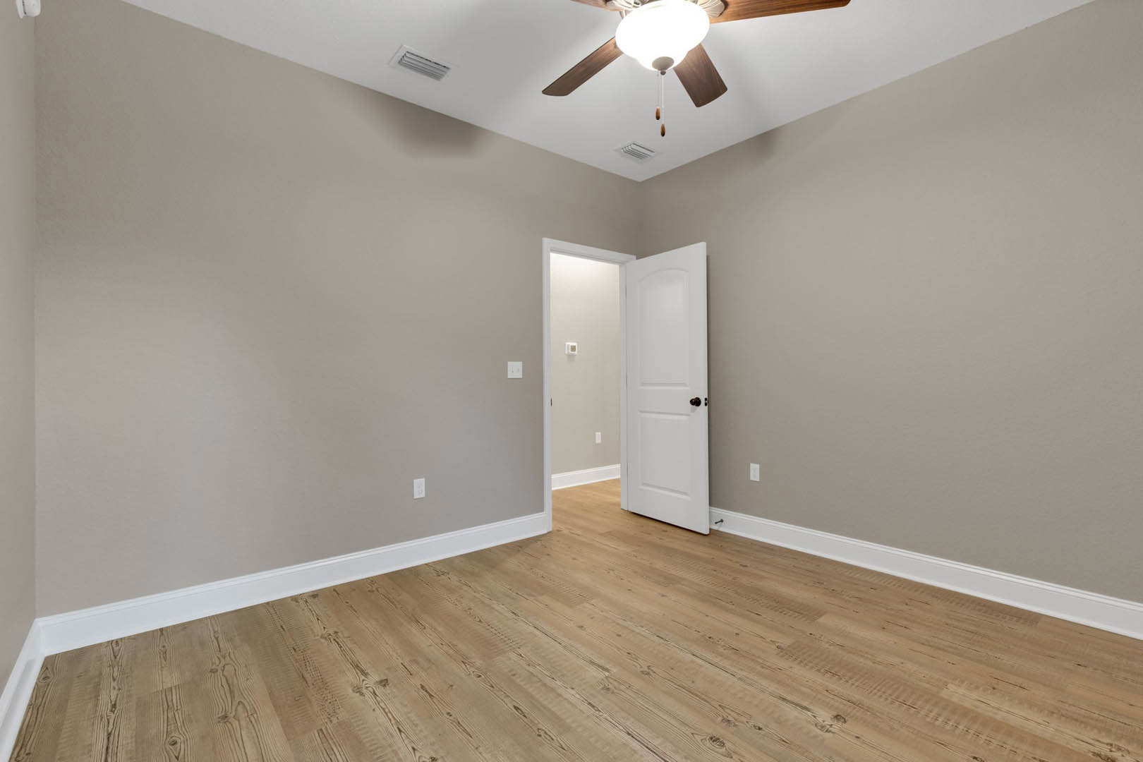 Wood flooring, white walls, white door with black knob, ceiling fan with light fixture, light switch and thermostat visible near door