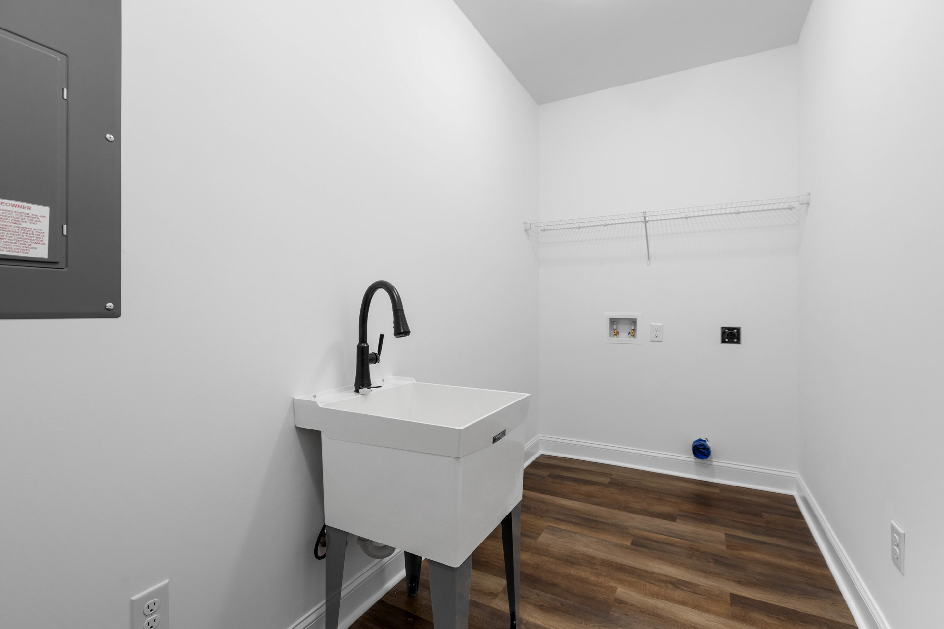 White porcelain sink with black faucet and metal legs against a white plaster wall, red-lettered sign mounted above.