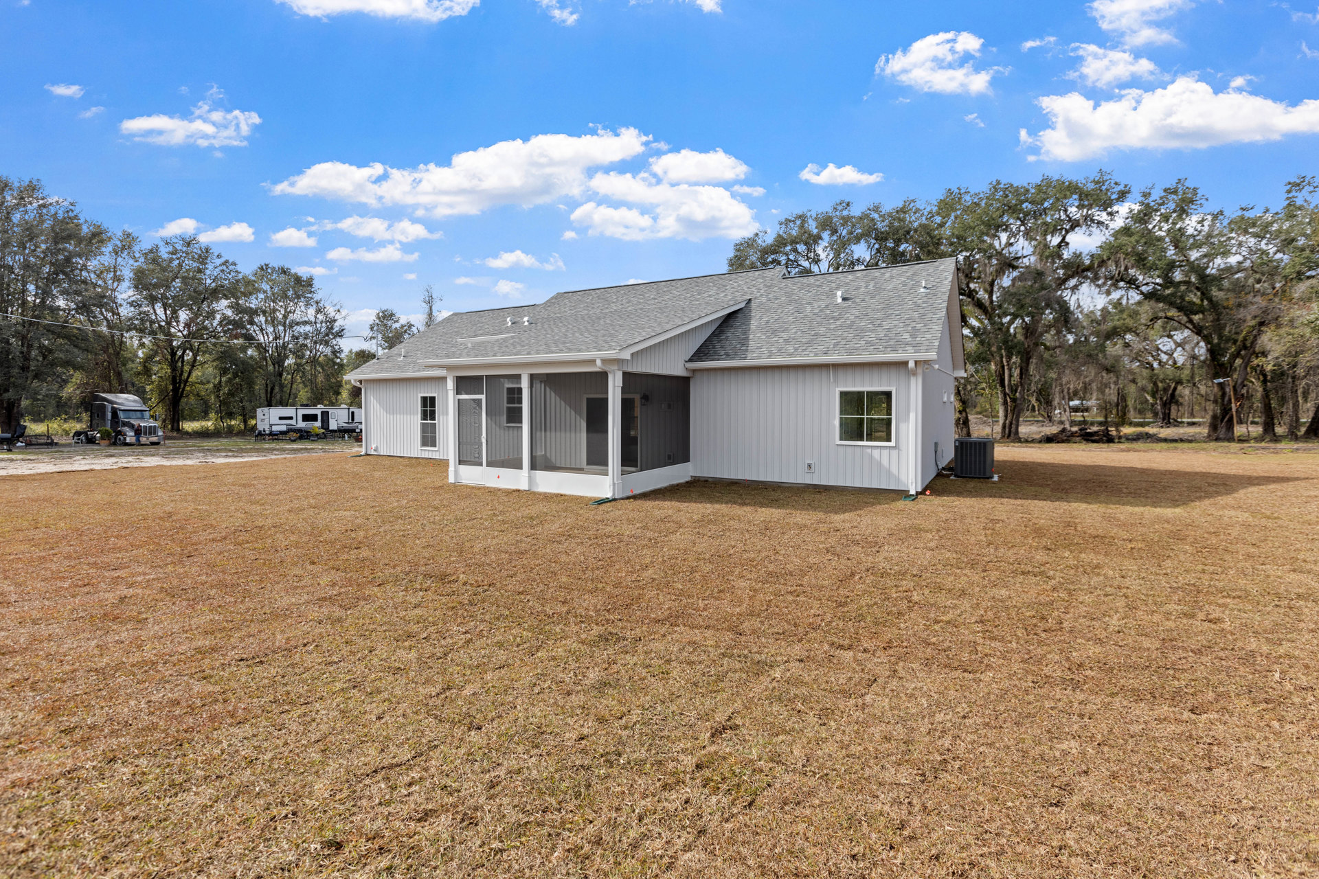 Two-story home with white-framed windows, screened porch, and shingled roof, surrounded by green grass and mature trees under a cloudy sky; large yard with a man standing beside a