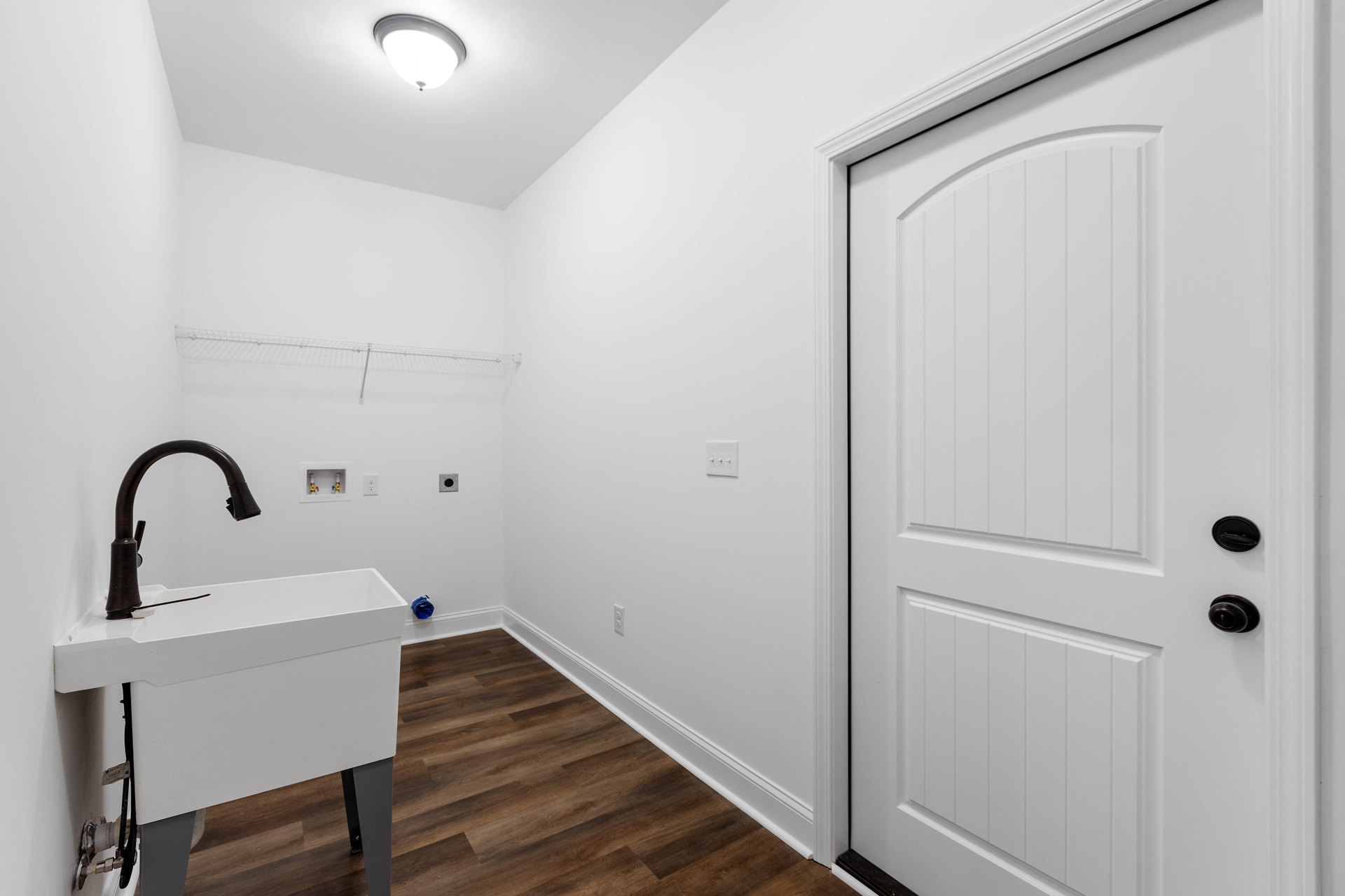 White bathroom with tile walls, white sink featuring a black faucet, white door with black hardware, and ceiling light fixture