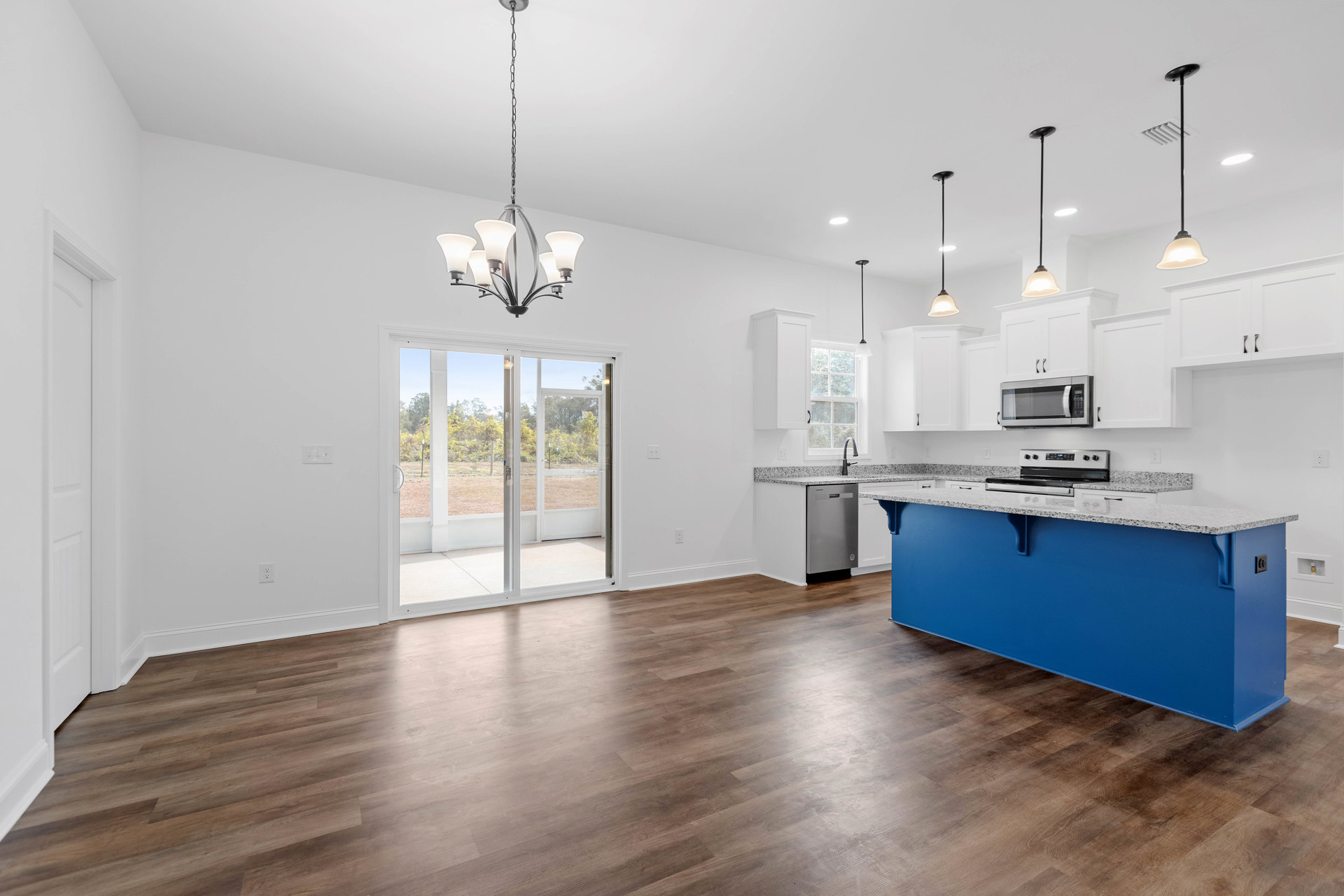 Blue kitchen island with white quartz countertop, wood flooring, stainless steel stove, open microwave, white cabinetry, sliding glass door, large window, and ceiling vent