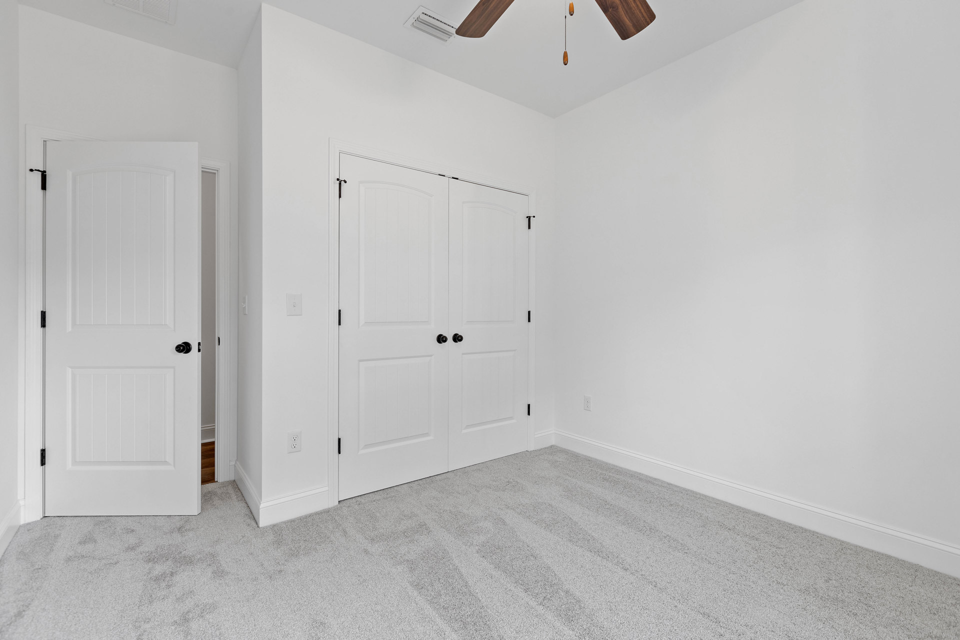 Carpeted room with white double doors featuring black knobs, ceiling fan, and light-colored walls