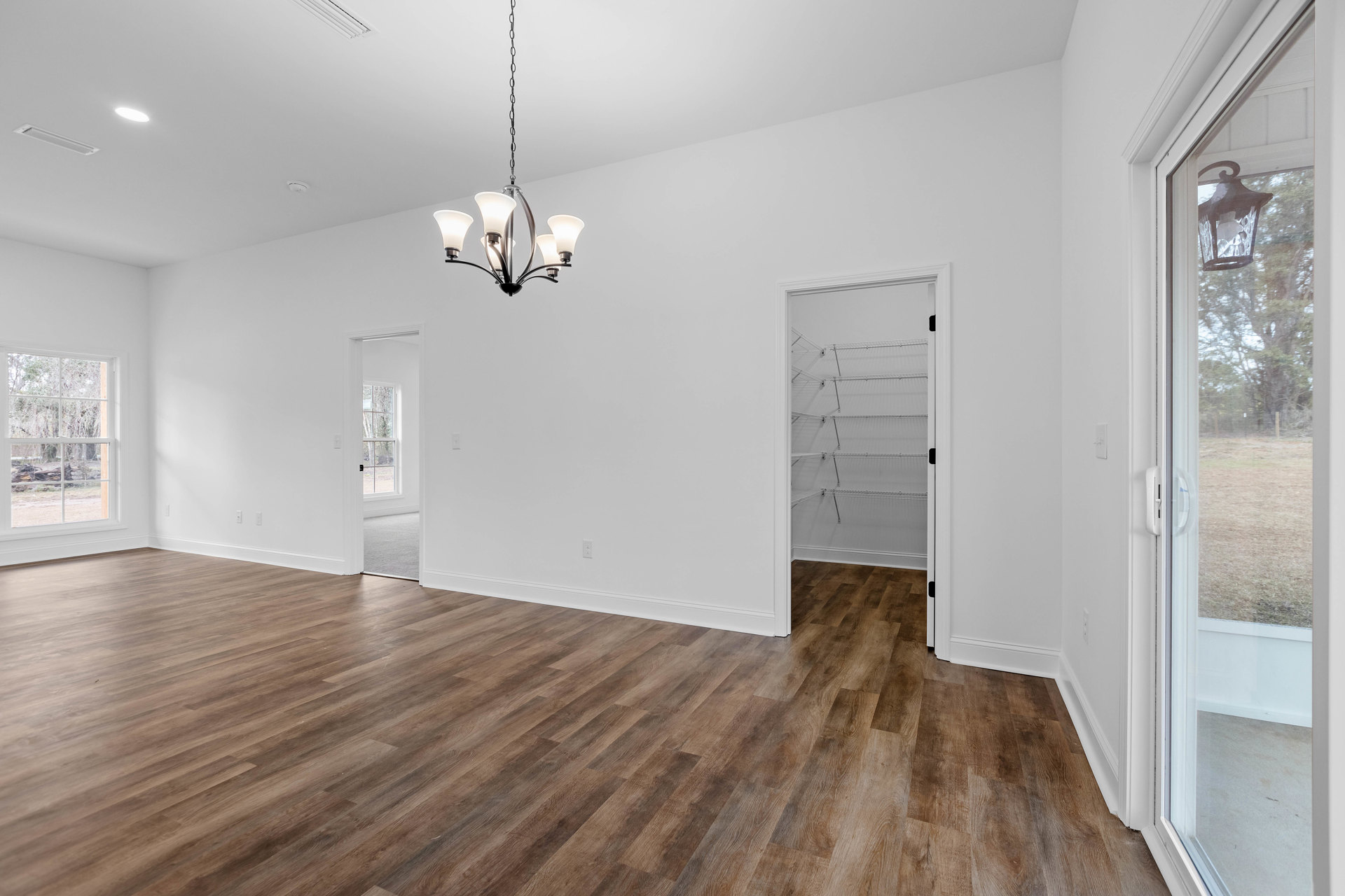 Wood plank flooring, white plaster walls, ornate chandelier with multiple bulbs, built-in shelving along one wall