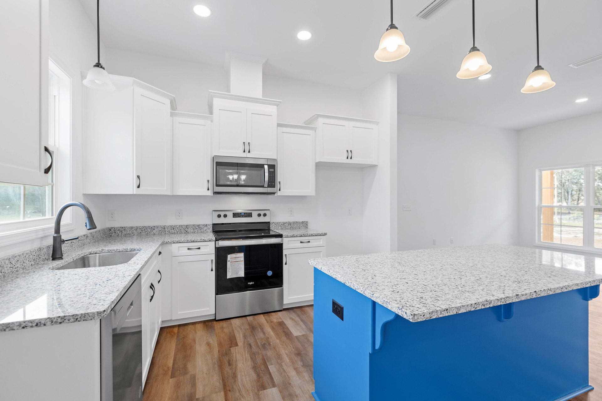 White cabinetry and blue island with quartz countertop, stainless steel appliances including microwave and oven, chrome faucet, and paper taped to window above stove.