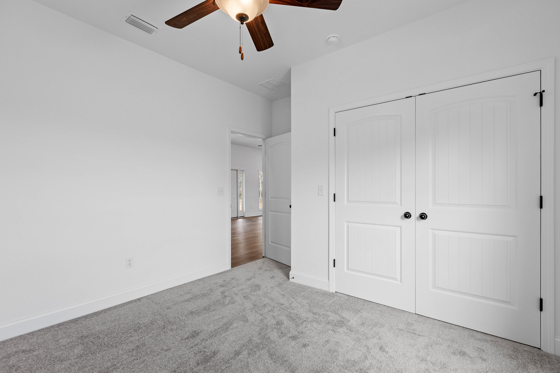 Ceiling fan with light fixture mounted above wood flooring, white double doors, and carpeted area in a residential room with plaster walls