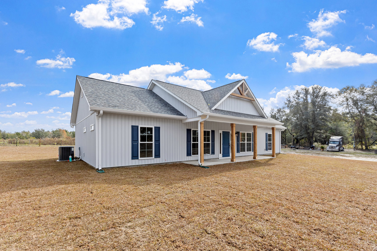 Two-story house with blue roof, white siding, covered front porch, blue window shutters, manicured lawn, mature trees, and pickup truck parked on driveway