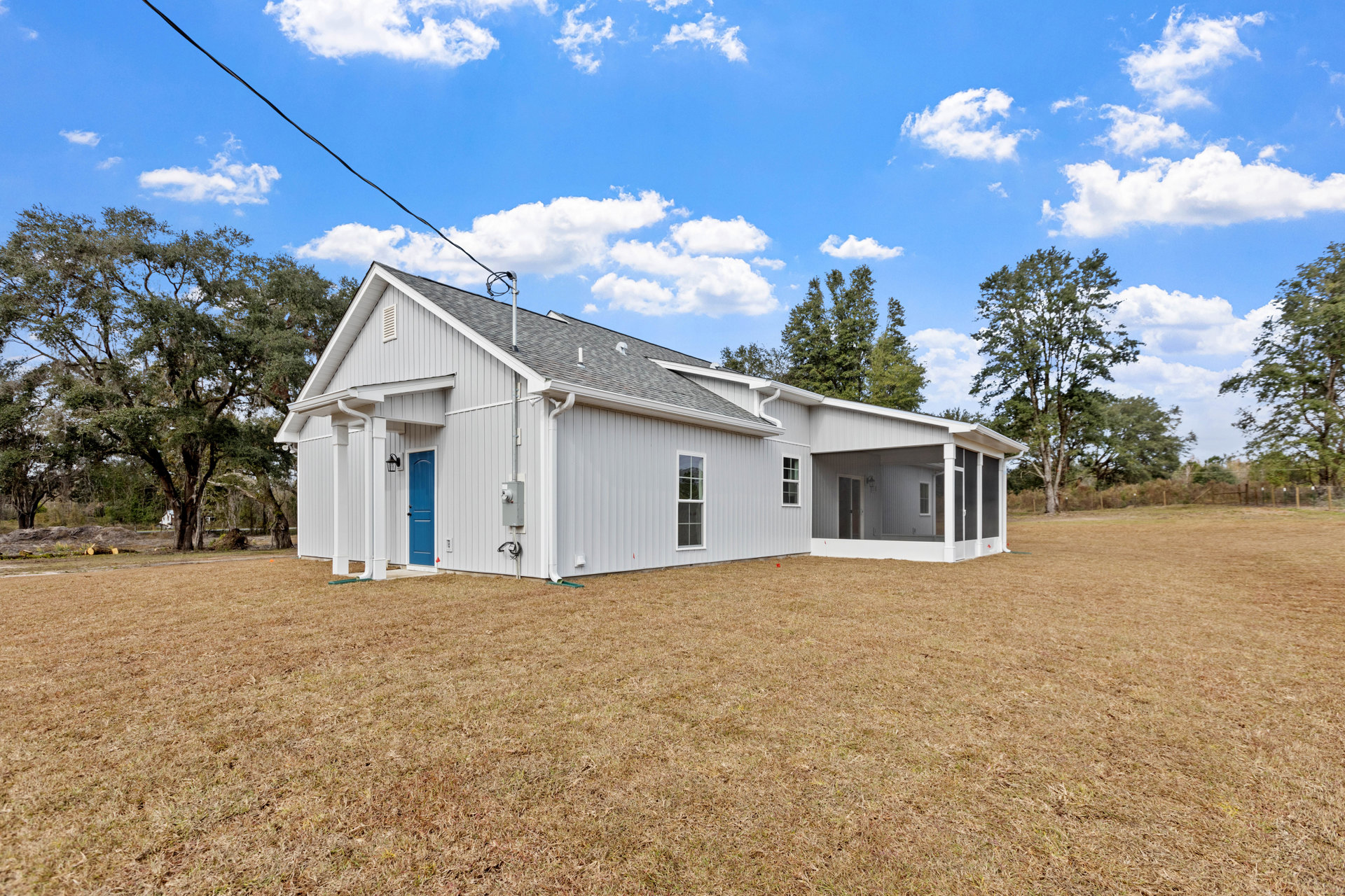 White house with grey roof, covered front porch, expansive green lawn, leafy tree, blue sky with scattered clouds