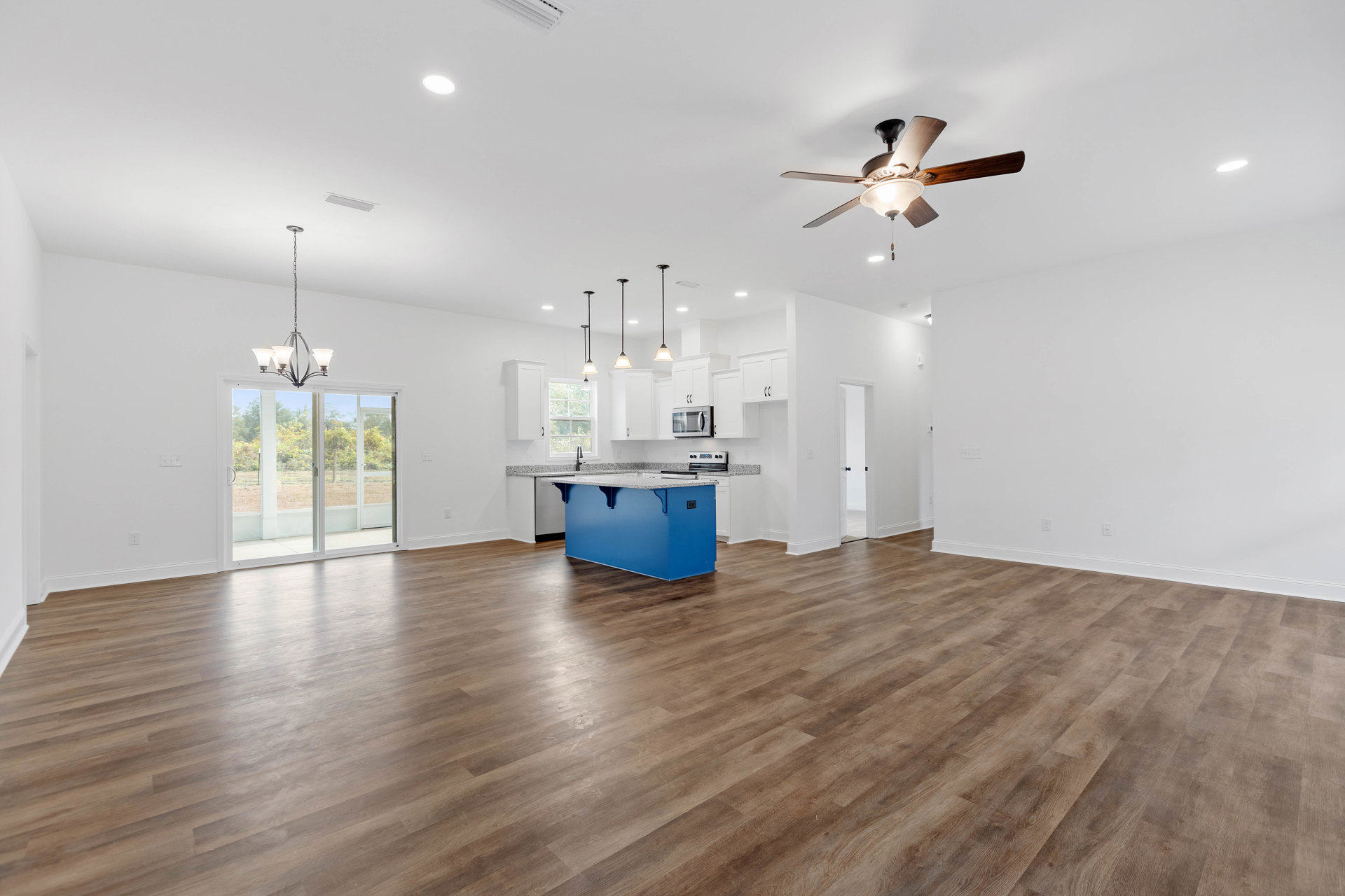 Open kitchen with blue island featuring marble countertop, wood flooring, ceiling fan with light fixture, glass door, and neutral plaster walls.