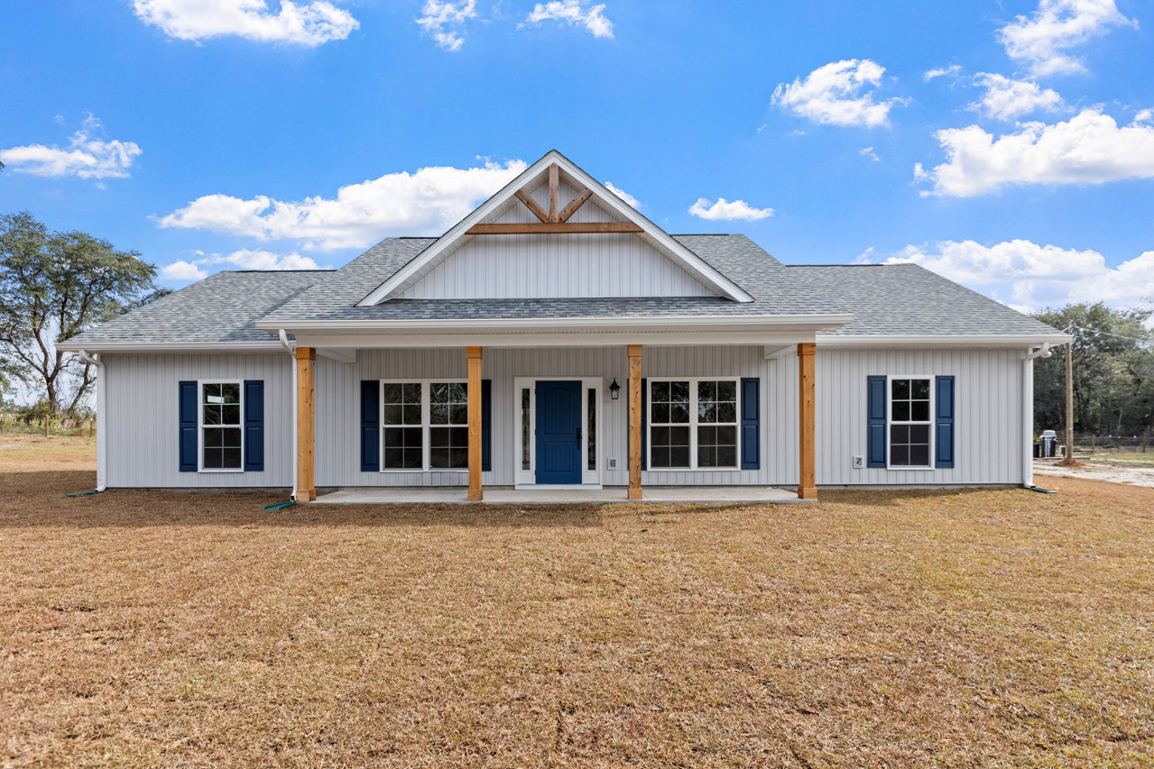 Two-story house with blue front door, white trim, blue window shutters, triangular roof, manicured green lawn, and clear blue sky