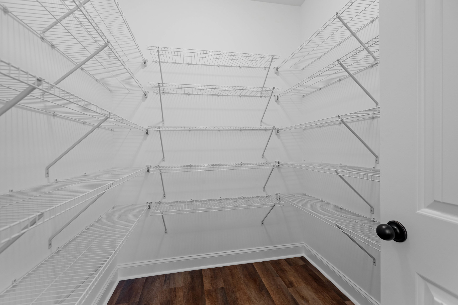White metal shelves mounted on a white plaster wall above light wood flooring with white baseboards; black balloon floating near shelves.
