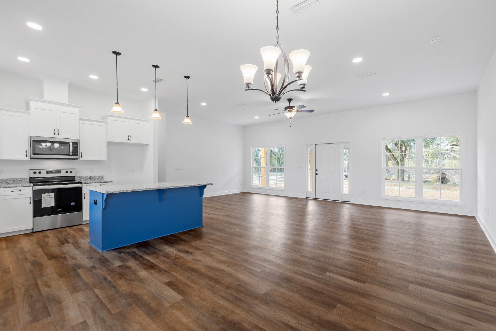 Kitchen with blue island featuring white countertop, wood flooring, stainless steel stove with paper on top, glass surface with paper, modern light fixture, and white cabinetry.
