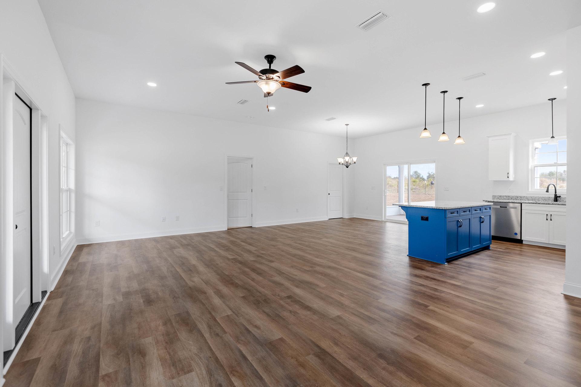 Open-concept room featuring wood flooring, white walls and doors, blue kitchen island with drawers, ceiling fan with light, and ceiling vent.