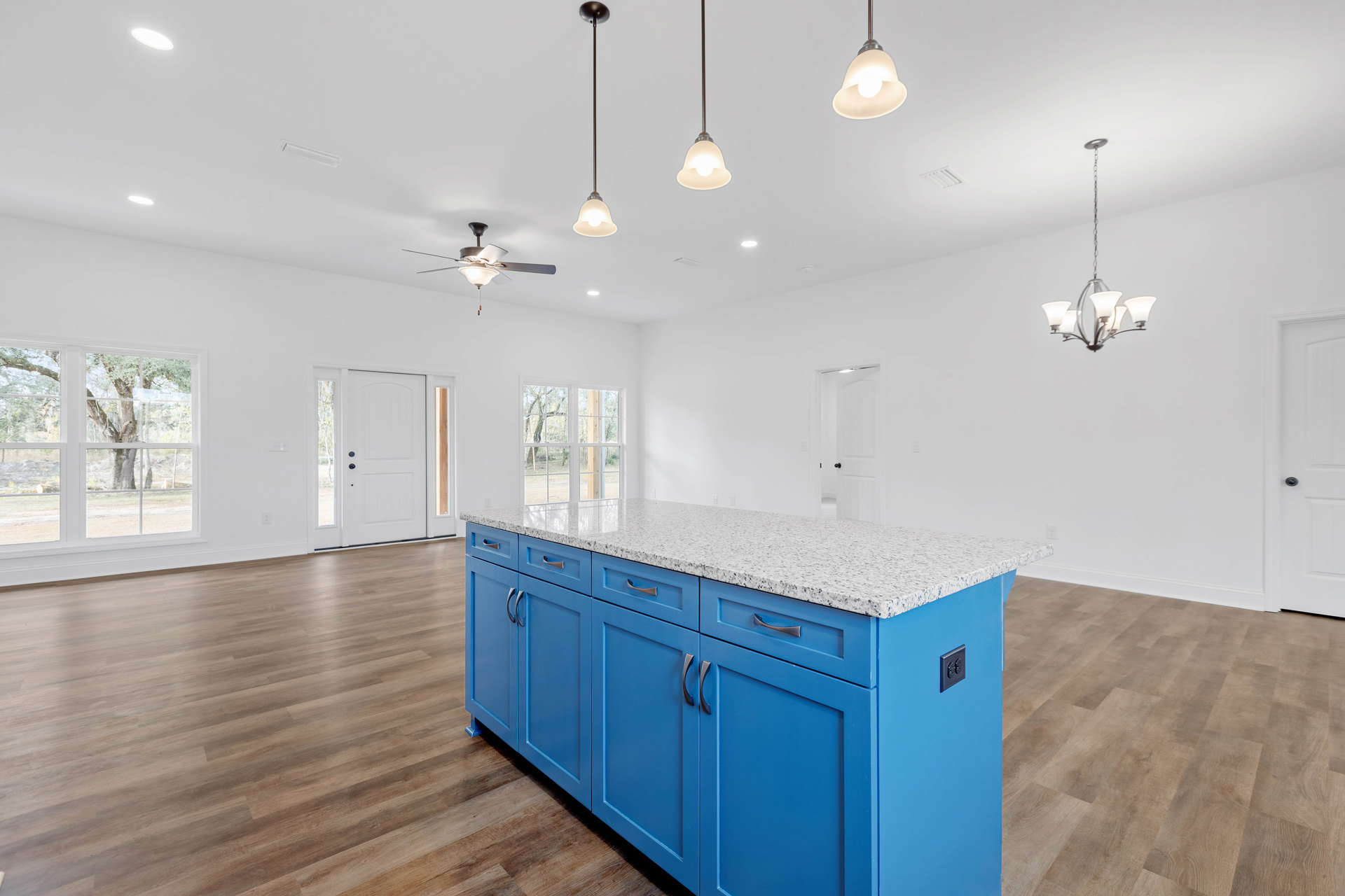 Blue kitchen island with matching cabinets and silver handles, white countertops, stainless steel sink, pendant light fixture hanging from ceiling, wood flooring, and a metal pole