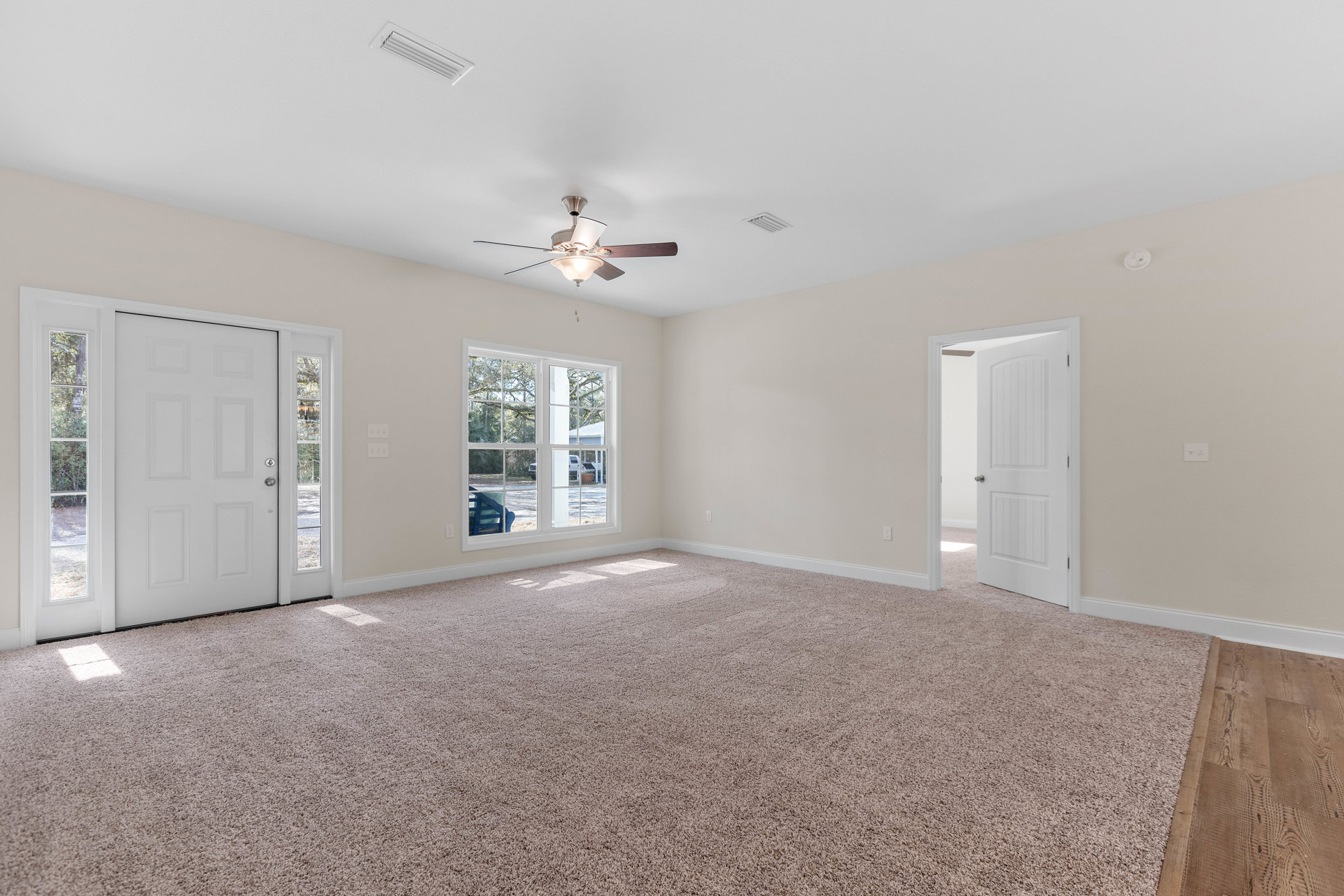 White walls and carpeted floor, ceiling fan with light fixture, wood floor section, white doors with silver knobs, blue chair positioned by a window