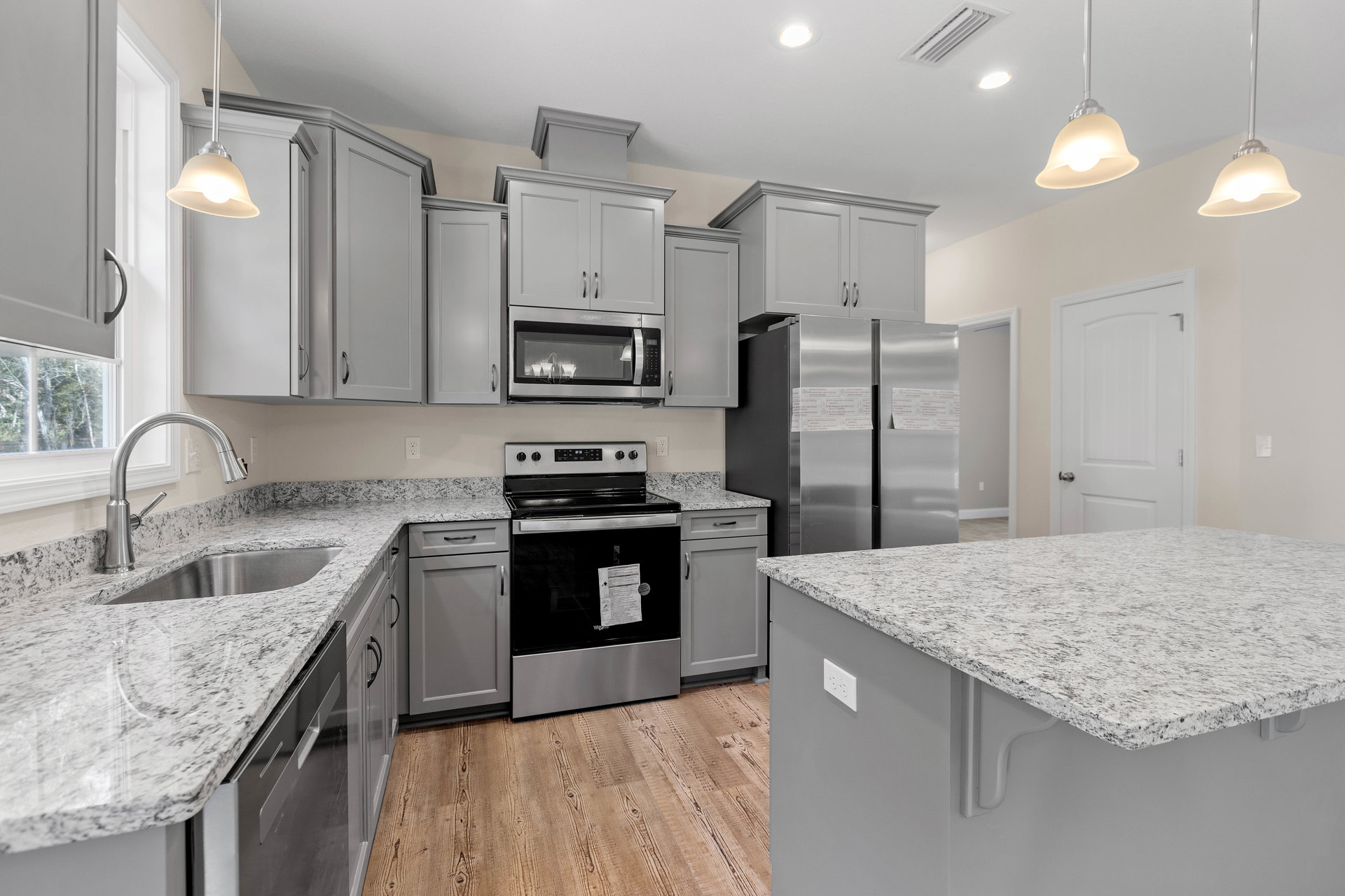 Granite countertops, stainless steel oven with paper taped to door, white surface island, built-in microwave with overhead light fixture, close-up stainless sink, ceiling pendant