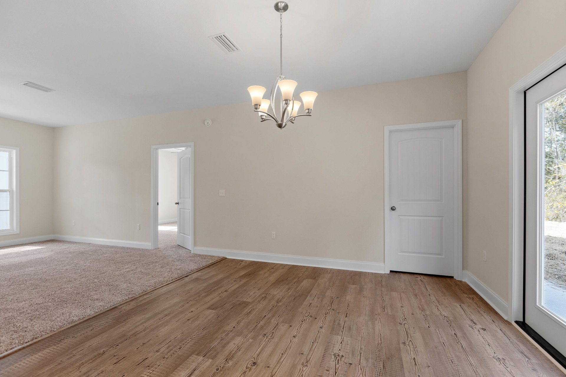 Chandelier with white shade hanging from plaster ceiling with vent, wood laminate flooring, white door with silver knob, window overlooking trees