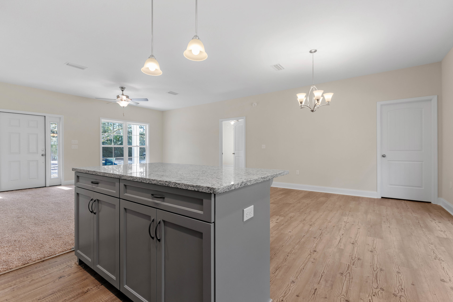 Marble kitchen countertop with stainless steel sink, white cabinetry, kitchen island with granite surface, silver knob on open white door, modern ceiling light fixture, hardwood
