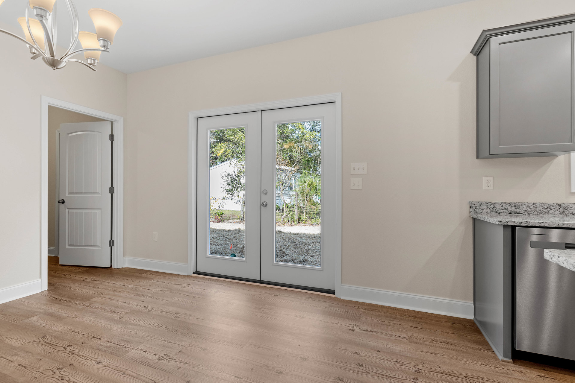 Wood floor room with glass-paneled double doors, white cabinetry in the corner, silver door knob, and chandelier overhead.
